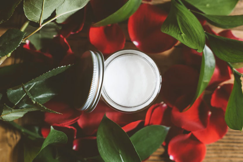 A jar of face cream surrounded by leaves