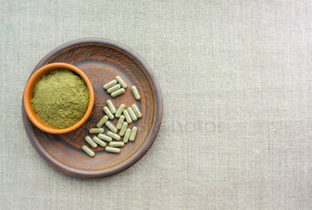 A photo of a bowl filled with kratom powder, sitting on top of a plate of kratom capsules.