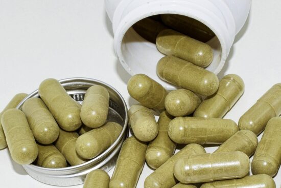 A pile of green kratom capsules sits on a white background