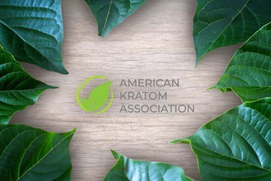 The American Kratom Association logo sits on a wood background, surrounded by leaves