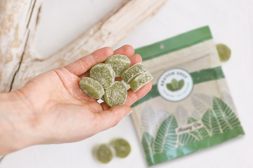 A hand holding a handful of green kratom edibles atop a bag of Kratom Spot kratom.