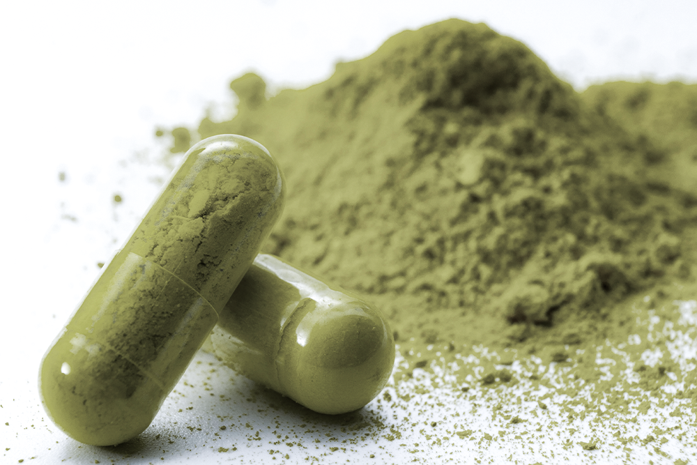 Two kratom capsules next to a pile of kratom powder