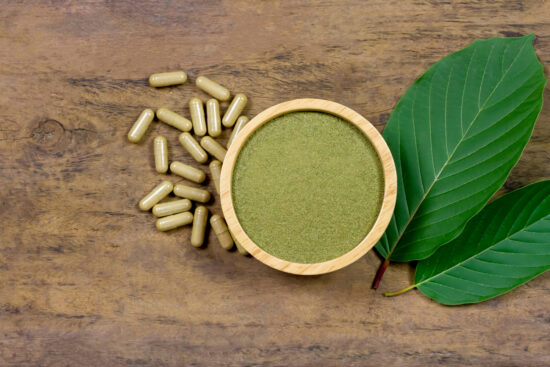 Kratom powder and capsules next to a kratom leaf.